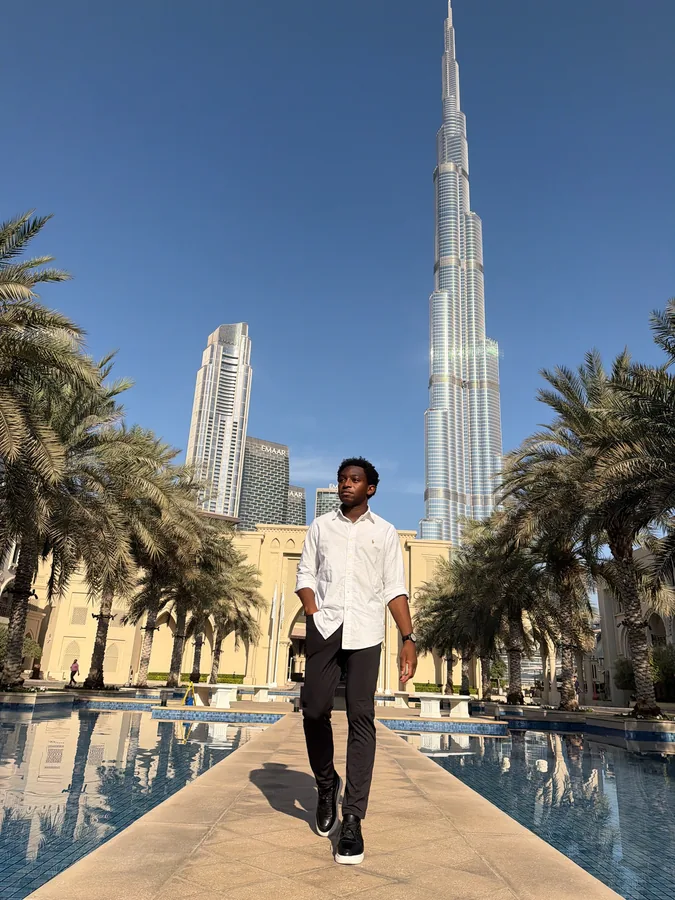 A traveler standing beneath the Burj Khalifa on a palm-lined walkway.