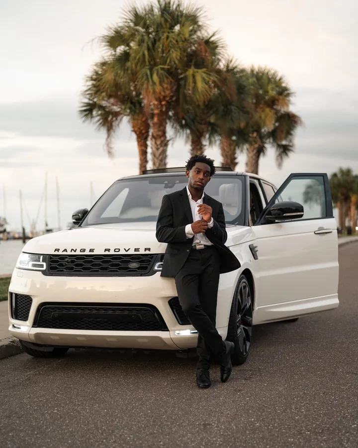 A traveler in a suit beside a white SUV and palm trees.