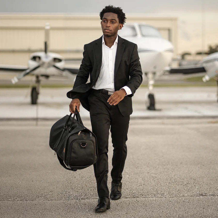 A suited traveler carrying a bag in front of a small airplane.