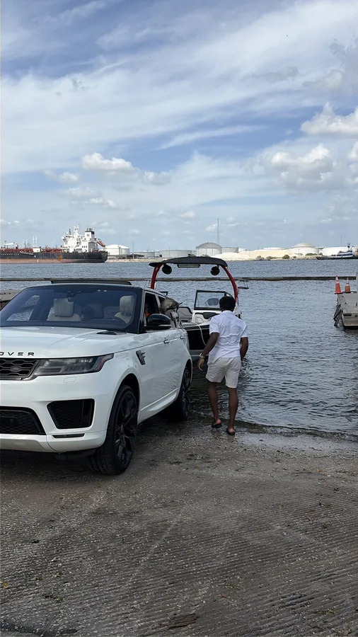 A person walking toward a boat beside a white SUV at the waterfront.