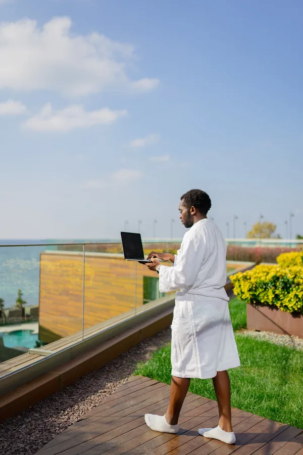 A traveler in a robe working at a laptop on an outdoor terrace.
