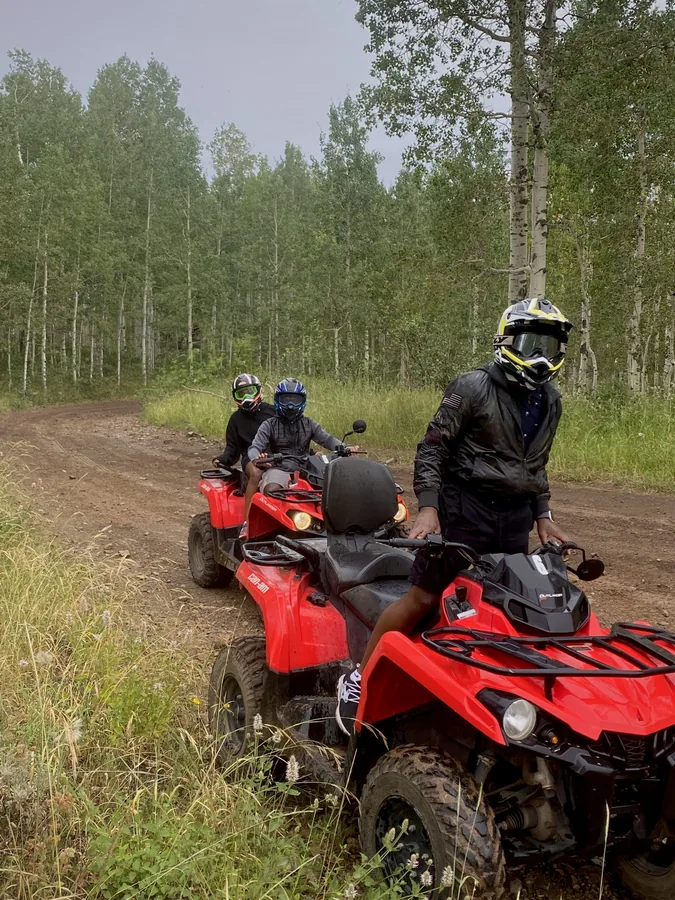 Two riders on red quad bikes beside a forest trail.