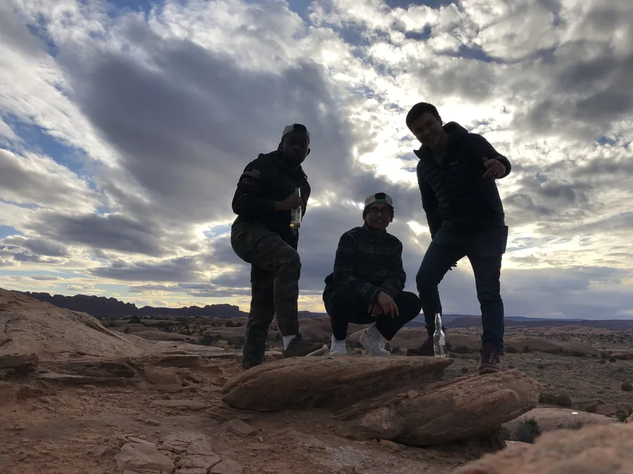 Three travelers on a rocky overlook under a dramatic sky.